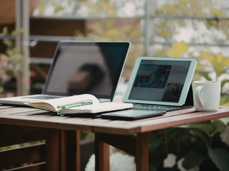 A quiet workspace with a laptop, notebook, and tablet near a window, reflecting nostalgia and quiet perseverance